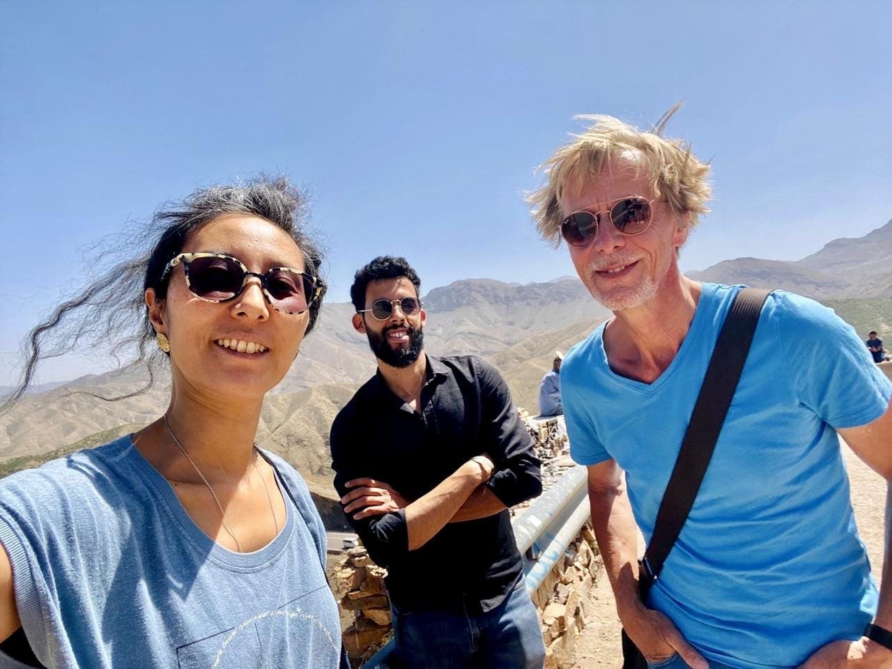Friends taking a selfie at a High Atlas viewpoint in spring, with green slopes and snow-capped peaks behind them