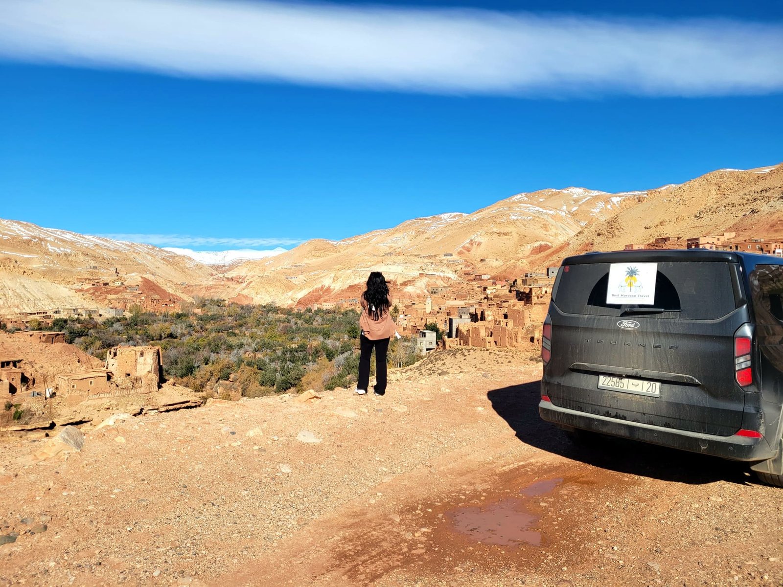 A private tour vehicle parked at a High Atlas viewpoint with snow-capped peaks behind it in January
